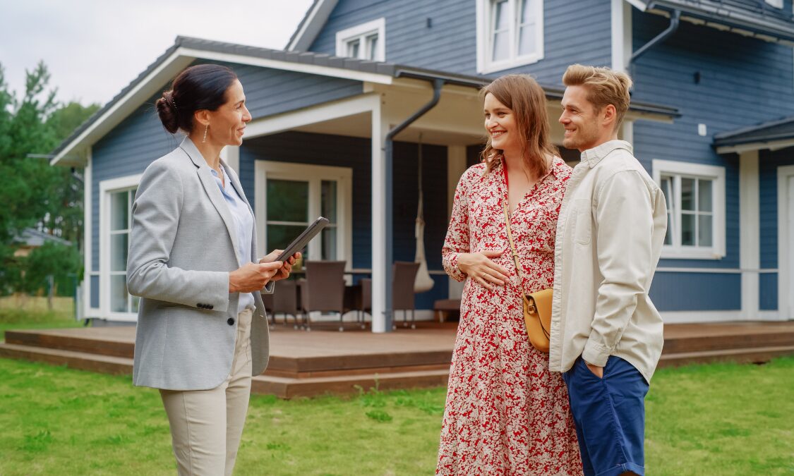 Estate agent speaking with a couple outside a modern UK home about growing a property portfolio and landlord compliance